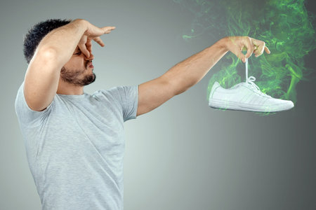 A man holds sneakers in his hands. Nasty smell. Stink legs, fungus on the legs.