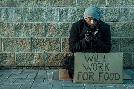 A man, homeless, a man asks for alms on the street with a sign will work for food. Concept of homeless person, addict, poverty, despairの写真素材