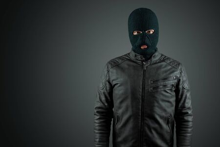 Robber, thug in a balaclava on a black background. Robbery, hacker, crime, theft. Copy spaceの写真素材