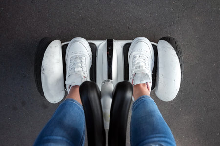 Legs of a girl in white sneakers on a white hoverboard, self-balancing scooter in a park close-up....