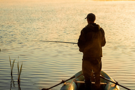 Male fisherman at dawn on the lake catches a fishing rod.