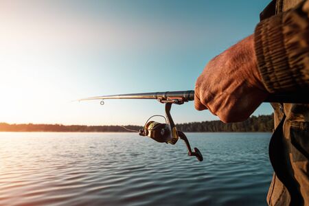 Hands of a man hold a fishing rod, a fisherman catches fish at dawn.の写真素材
