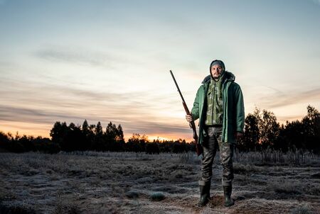 Hunter man in camouflage with a gun during the hunt in search of wild birds or game on a beautiful sunset. The concept of a hobby, killing. copy space.の写真素材