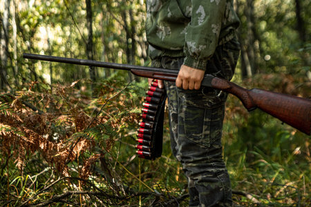 A hunter with a gun in his hands in hunting clothes in the autumn forest close-up. The hunting...