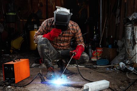 A male welder in a welding mask works with an arc electrode in his garage. Welding, construction, metal workの写真素材