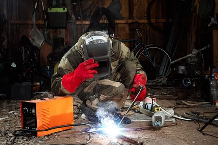 A male welder in a welding mask works with an arc electrode in his garage. Welding, construction, metal workの写真素材