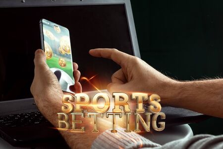Smartphone in hand gold lettering Sports Betting on laptop background. Bets, sports betting, bookmaker. Mixed media.の写真素材