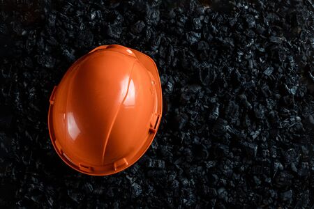 An orange helmet of a miner lies on a heap of coal, open pit coal mining, copy space. Fossil fuels, environmental pollutionの写真素材