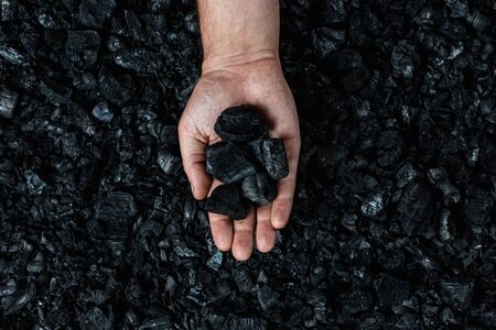 Male hand with coal on the background of a heap of coal, coal mining in an open pit quarry, copy space. Fossil fuels, environmental pollutionの写真素材