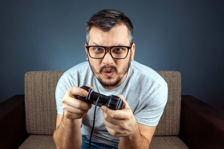 A man plays a video game console while sitting on a sofa. Day off, entertainment, leisureの写真素材