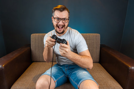 A man plays the console, video games react strongly and emotionally while sitting on the couch. Day...