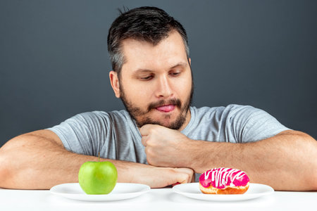 An adult man chooses between a donut and a green apple. Concept Resistance to temptation, fast food,...