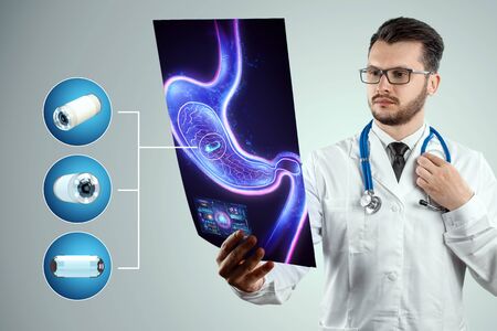 Doctor against the background of a hologram of the stomach, A camera the size of a capsule in the stomach, an endoscopy procedure. Digestive tract disease concept. Mixed medium, copy spaceの写真素材