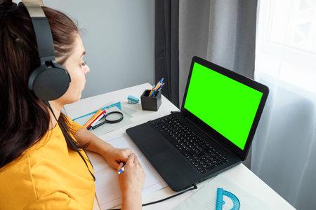 Pretty girl uses laptop with green screen, mockup concept. Watching a webinar, looking for friends...