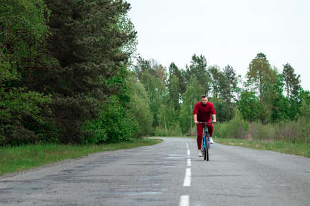 A man in a tracksuit on a bicycle rides on a road in the forest. The concept of a healthy lifestyle, cardio training. Copyspaceの写真素材