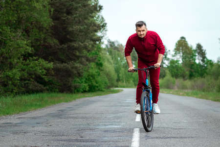 A man in a tracksuit on a bicycle rides on a road in the forest. The concept of a healthy lifestyle, cardio training. Copyspaceの写真素材