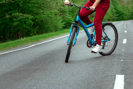 A man in a tracksuit stands next to a bicycle on a road in the forest. The concept of a healthy...