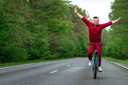 A man in a tracksuit rides a bicycle without hands on the road in the forest. The concept of a healthy lifestyle, cardio training. Copyspaceの写真素材