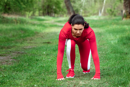 A girl in a tracksuit is preparing to run, physical exercises against the backdrop of nature,...