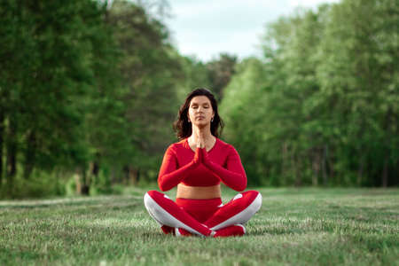 A girl in a tracksuit sits in a lotus position, ega on a background of nature. The concept of a healthy lifestyle, exercise, fresh air. Copy spaceの写真素材