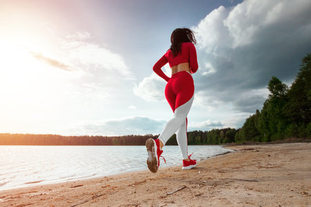 A beautiful, happy girl in a tracksuit runs along the path of a lake or sea. The concept of a...