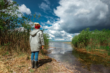 A boy in a hat from the back against the backdrop of a summer lake