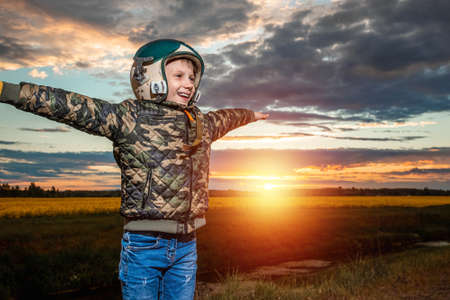 A boy in a pilot's helmet on a sunset background. Dream concept, choice of profession, game. Copy spaceの写真素材
