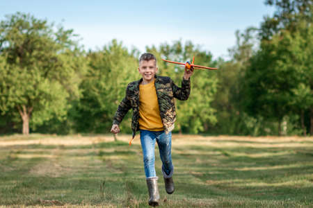 A boy runs across the field and launches a toy airplane against the backdrop of greenery. The concept of dreams, choice of profession, pilot, childhood. Copy spaceの写真素材