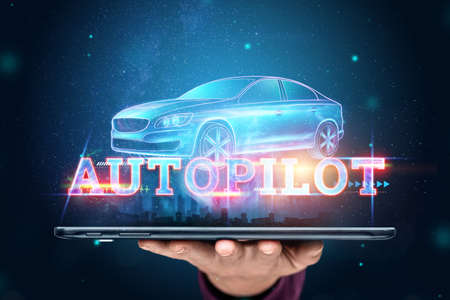 The hand of a man with a tablet and the inscription Autopilot, the car automatically detects the road and obstacles, scans the road. transport technologies. Hologram, copy spaceの写真素材