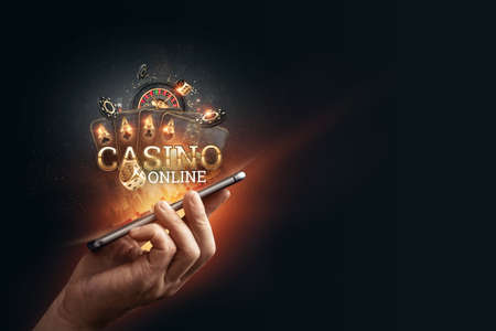 In a man's hand a smartphone with playing cards roulette and chips, black-gold background. Concept of online gambling, online casino. Copy space.の写真素材