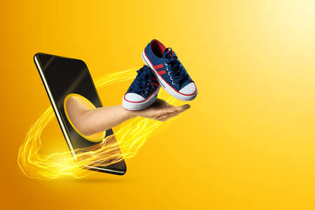 Hand gives sneakers for training via smartphone on a yellow background. Concept sports training online, stay at home, coach servicesの写真素材