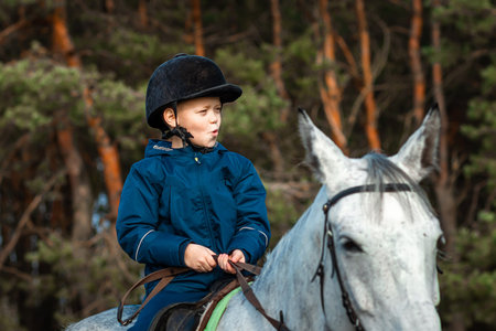 Little boy in a jockey cap on a white adult horse on a background of nature. Jockey, hippodrome,...