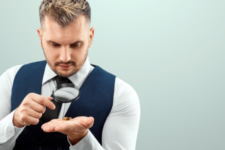 A man looks through a magnifying glass at a stack of coins in his palm. Small salary, financial crisis, bankruptcyの写真素材