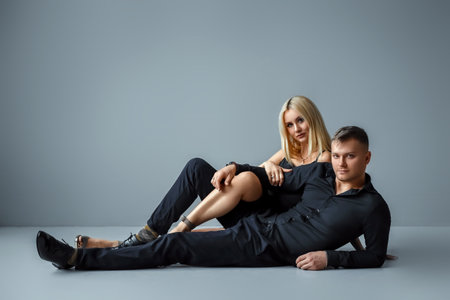 Beautiful young stylish European couple, man and woman, in black evening dresses on a gray backgroundの写真素材
