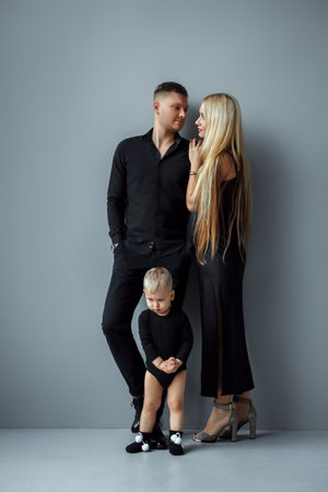 Photo of a beautiful European married couple, a young girl and a guy with a little son, posing together in front of the camera. Gray background, concept of modern family, family relationshipsの写真素材
