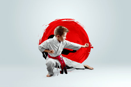 Full-length portrait of a boy in a white kimono with a red belt against the background of a red circle. Karate concept, training, goal, training, achievementの写真素材