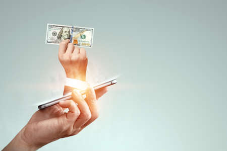 A businessman's hand crawls out of the smartphone screen with a one hundred dollar bill. Concept of money transfers, internet banking work onlineの写真素材