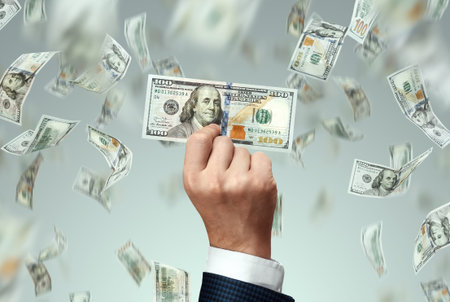 Businessman's hand holding a hundred dollar bill and falling dollars, start-up. The concept of...