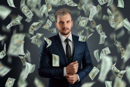 A businessman in a suit stands against the background of falling dollars. The concept of investments, dividends, interest, bank depositsの写真素材