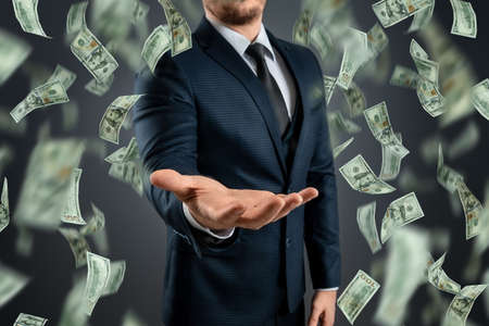 A businessman in a suit catches the falling dollars. The concept of investments, dividends, interest, bank depositsの写真素材