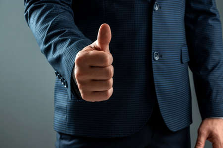 Male hand in suit shows thumbs up gesture on gray background. Concept ok, approval, close-upの写真素材