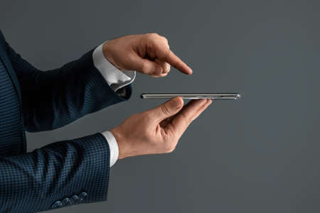 Hands of a businessman in a business suit holds a smartphone horizontally side view and presses the screen with his finger. Close-upの写真素材