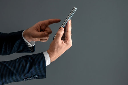 Hands of a businessman in a business suit holds a smartphone horizontally side view and presses the...