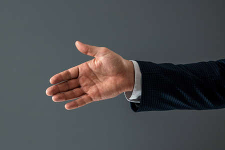 Male hand in suit shows thumbs up gesture on gray background. Concept ok, approval, close-upの写真素材
