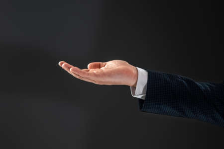 Male hand in a suit shows a palm up gesture on a gray background. Concept of request, bankruptcy, close-upの写真素材