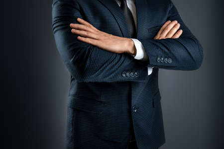 A man in a business suit stands with his arms crossed on a gray background. Concept businessman, business communication. Close-upの写真素材