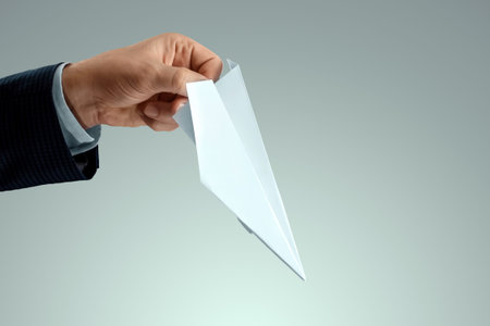 A man's hand in a business suit holds a paper airplane. Startup concept, light business, getting...