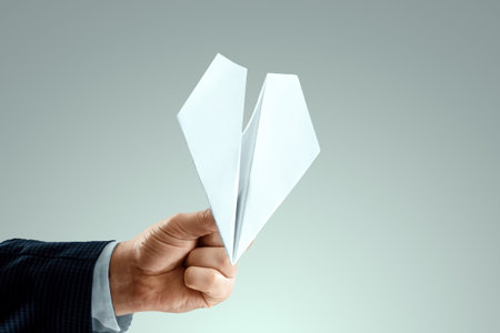 A man's hand in a business suit holds a paper airplane. Startup concept, light business, getting...