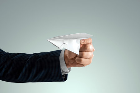 A man's hand in a business suit holds a paper airplane. Startup concept, light business, getting...