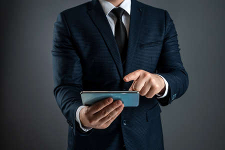 A businessman in a business suit holds a smartphone in his hands. Uses the Internet to work and communicate with partners. Online business concept, remote work, freelance. Close-upの写真素材
